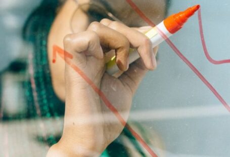Data-Driven Strategies - Woman in a Beige Coat Writing on a Glass Panel Using a Whiteboard Marker