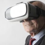 Wearable Devices - Smiling elderly gentleman wearing classy suit experiencing virtual reality while using modern headset on white background