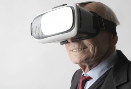 Wearable Devices - Smiling elderly gentleman wearing classy suit experiencing virtual reality while using modern headset on white background