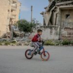 Disruption - Full body side view of boy in casual clothing riding on bicycle along old ruined construction in daytime