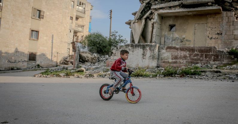 Disruption - Full body side view of boy in casual clothing riding on bicycle along old ruined construction in daytime