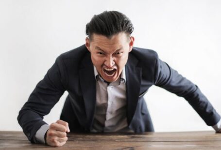 Human Error - Expressive angry businessman in formal suit looking at camera and screaming with madness while hitting desk with fist