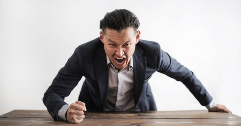 Human Error - Expressive angry businessman in formal suit looking at camera and screaming with madness while hitting desk with fist